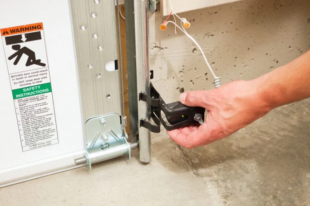 Hand inspecting a garage door safety sensor mounted near the floor